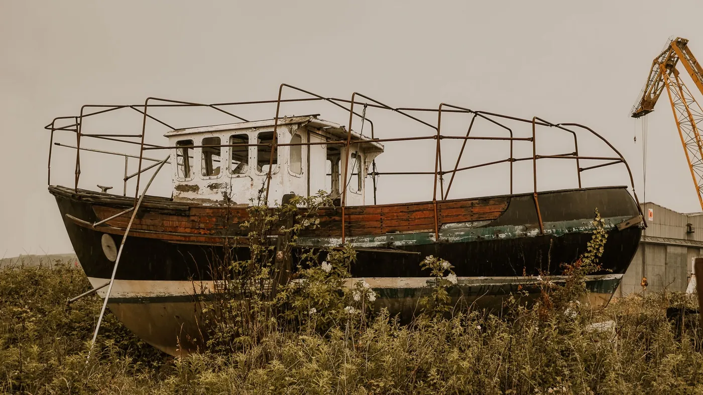 A stripped-out hull sitting in long grass with its frames exposed