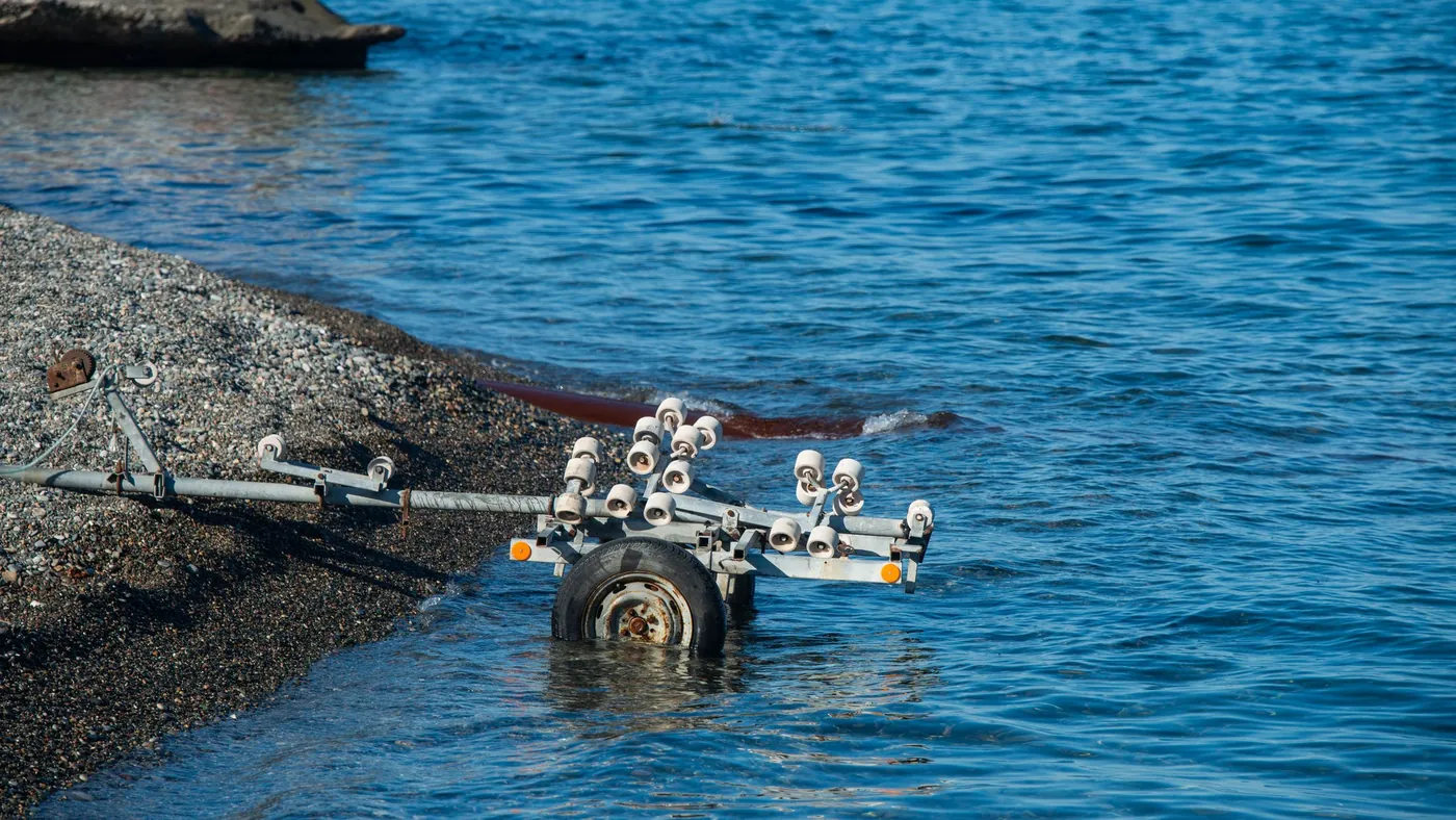 An empty roller trailer backed halfway into the water at a launch ramp