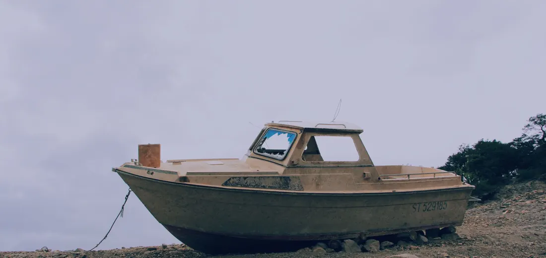 A tired older runabout beached on a rocky shore